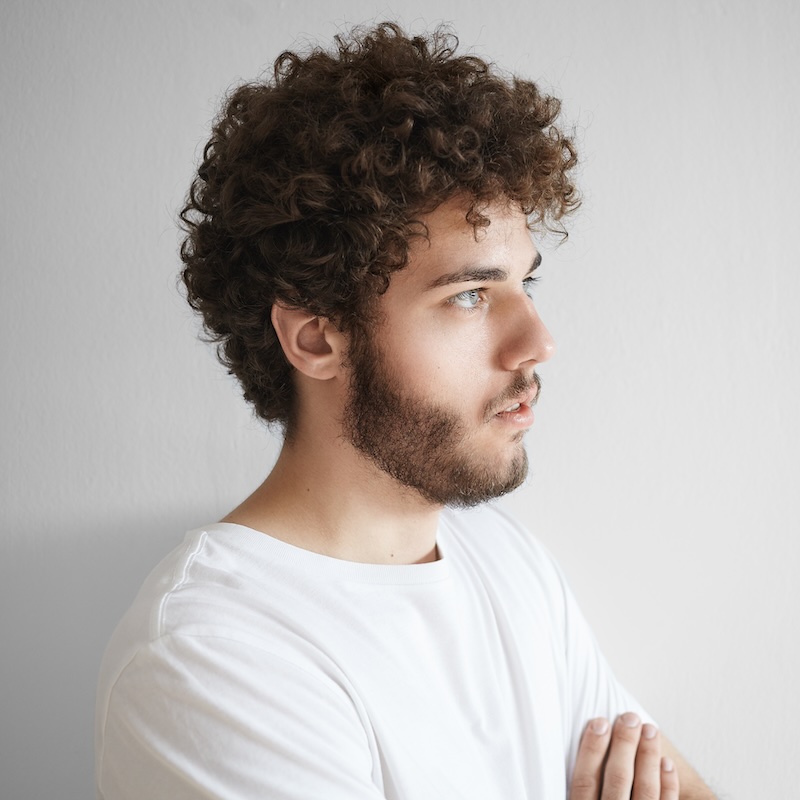 Close portrait of attractive young Caucasian male with curly hair, thick beard and beautiful features posing isolated in studio with blank copy space wall for your text or promotional information